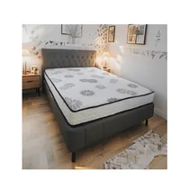 Matelas MEGALUX M-181419MM blanc avec un motif floral gris et un liseré noir, posé sur un lit gris dans une chambre à coucher moderne et lumineuse. Des coussins et des lampes de chevet complètent le décor