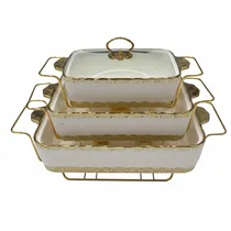 Ensemble de trois plats chauffants rectangulaires en céramique blanche et dorée empilés.